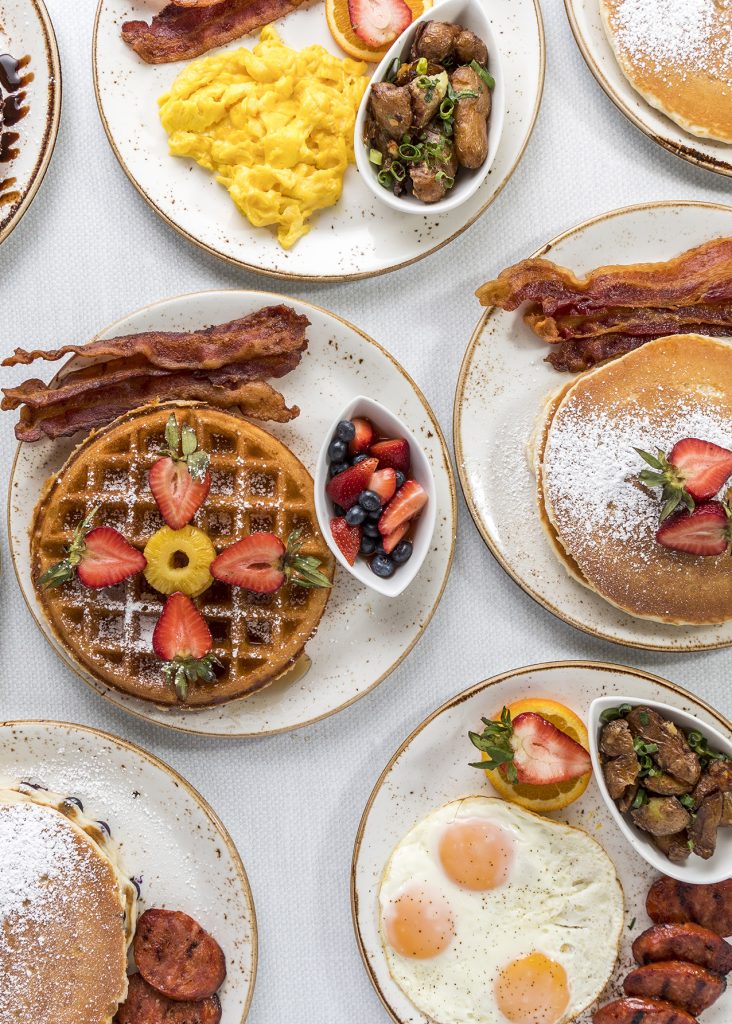 a variety of breakfast dishes, like waffles, pancakes, eggs, and omelets on a table spread in Waikiki, Hawaii